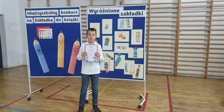 Powiększ grafikę: Chłopiec stojący na tle tablicy z nagrodzonymi pracami